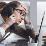 Woman sitting at a desk on the phone staring at computer and looking stressed out